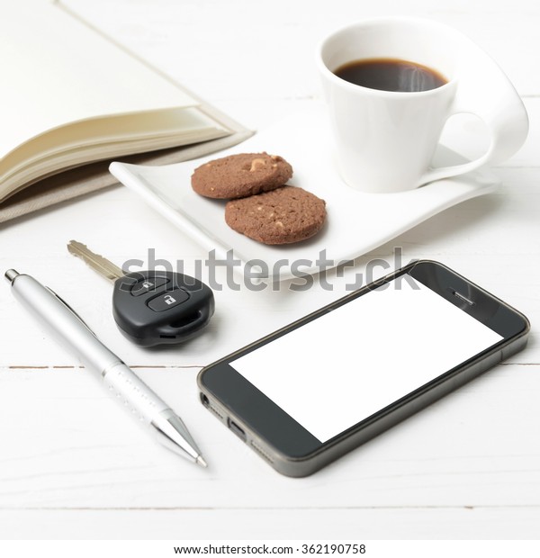 coffee cup with cookie,phone,open notebook and car\
key on white wood table