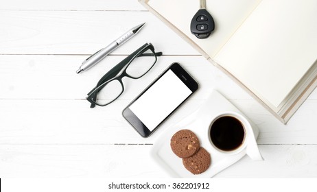 coffee cup with cookie,phone,open notebook,car key and eyeglasses on white wood table