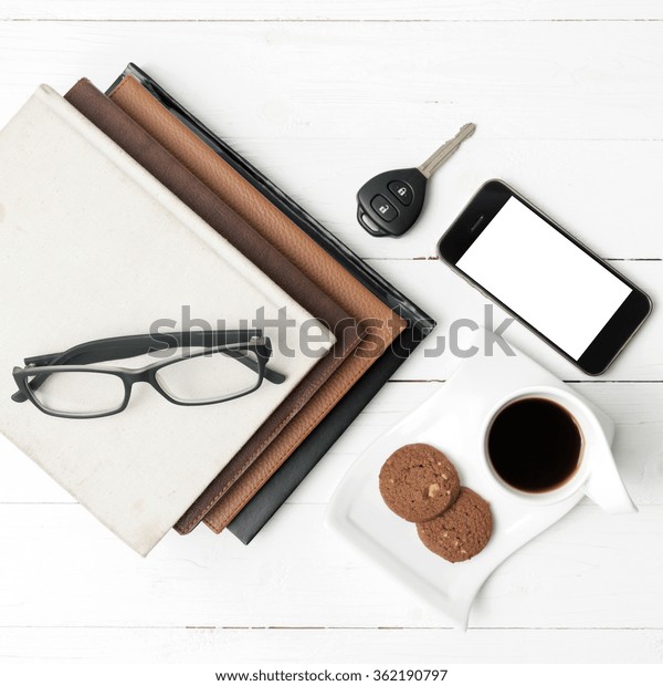coffee cup with cookie,phone,stack of book and car
key on white wood table
