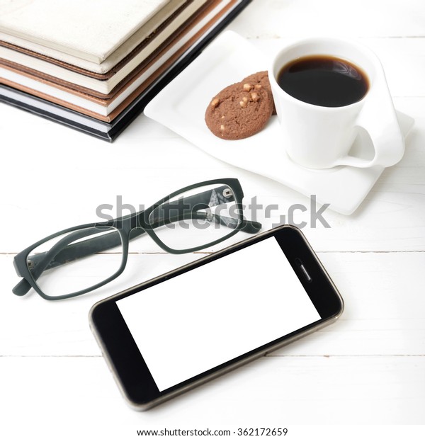 coffee cup with cookie,phone,stack of book and\
eyeglasses on white wood\
table