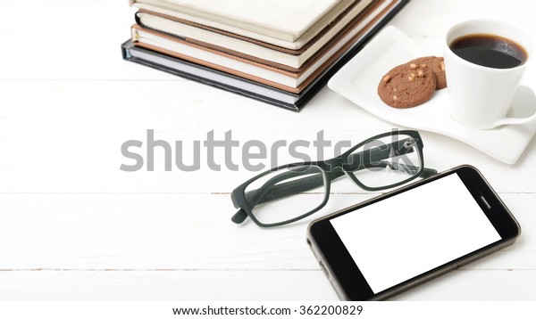 coffee cup with cookie,phone,stack of book and\
eyeglasses on white wood\
table