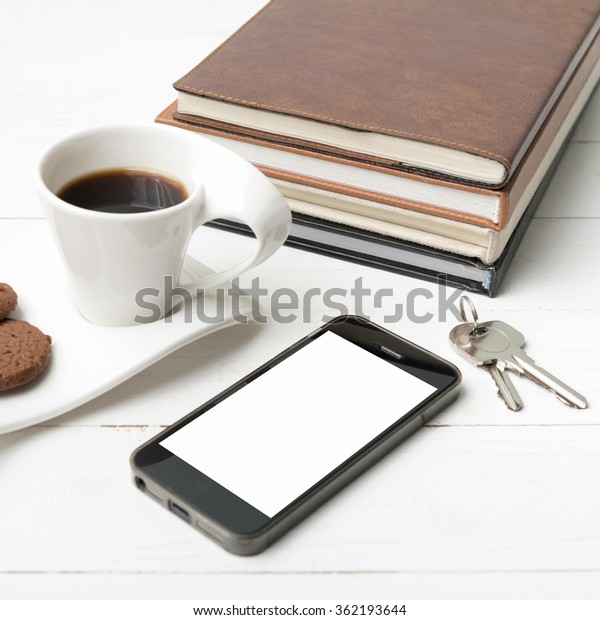 coffee cup with cookie,phone,stack of book and key\
on white wood table
