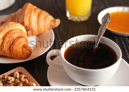 Coffee cup with croissant on a rustic dark wooden table. Food series. Two tasty fresh croissants, jam, orange juice. Continental breakfast served with freshly baked pastry. Close up view. Good morning