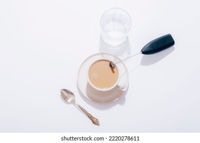 Coffee Cup, Glass Of Water, Spoon And Black Milk Frother On White Table. Top View, Flat Lay.