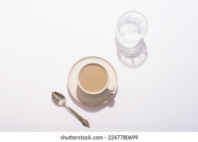Coffee cup, glass of water and spoon on white table in sunlight. Top view, flat lay.