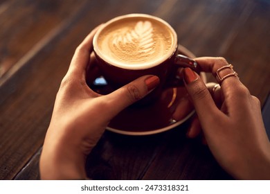 Coffee cup, hands and woman with latte art, caffeine and restaurant for cappuccino. Customer, hospitality and milk with foam for female person, morning and barista for breakfast in store or cafe