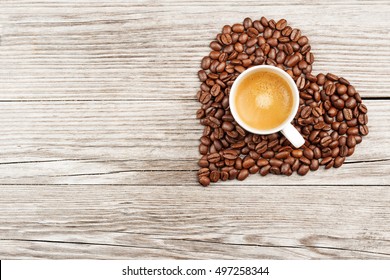 Coffee Cup In A Heart Of Beans On Wooden Table