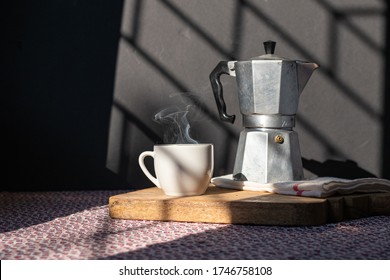 Coffee Cup And Italian Coffee Maker Over Table, Under Morning Light. Wood Tray, Hot Smoke From Cup. At Home Morning Rituals Concept. Lifestyle Food Background.