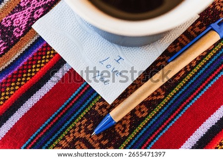 Coffee cup with a note written that says I love you on a colorful Inca woven table