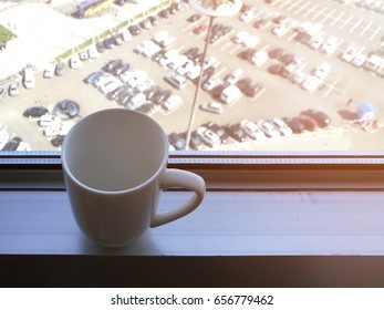 Coffee Cup On Aluminum Window Sill; In A Room At High Level Floor Of A Building; Car Park View In Background