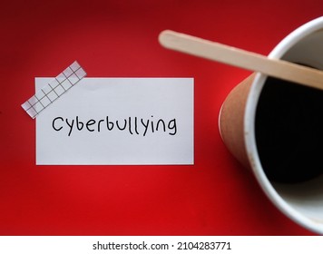 Coffee cup on red background with handwritten text note CYBERBULLYING, bullying over social media posting or sharing mean negative harmful personal content online causing embarrassment or humiliation - Shutterstock ID 2104283771