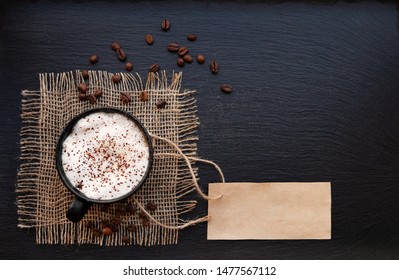 Coffee cup on rustic burlap and blank paper card. Top view with copyspace for your text. black background, cappuccino. price tag