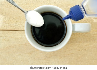 Coffee Cup On A Wood Table Seen From High Angle With A Spoon With Sugar On The Left And A Sweetener Bottle On The Right Side