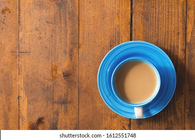 Coffee Cup On A Wooden Table From Above. Light Blue Coffee Cup On Wooden Background. Fresh Coffee With Milk In Blue Coffee Mug And Saucer On Wooden Background On A Minimalistic Photography. Top View.