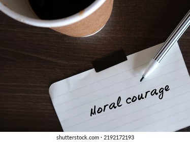 Coffee Cup And Pen Writing Words MORAL COURAGE, Means Courage To Take Action For Moral Reasons Or Act Upon Ethical Values To Help Others During Difficult Ethical Dilemmas