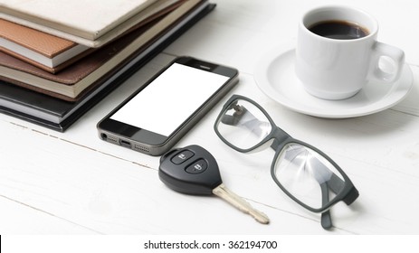 coffee cup with phone, car key,eyeglasses and stack of book on white wood table