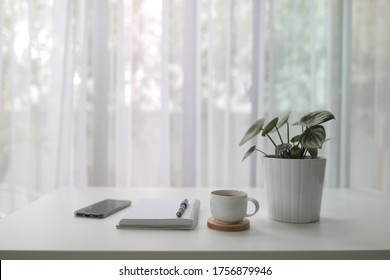 Coffee Cup With Plant And Notebook Pen And Phone On White Desk With See Through Curtain 