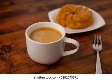 Coffee Cup With Round Lemon Cake On White Plate In Background And Dessert Fork On Brown Wooden Table.