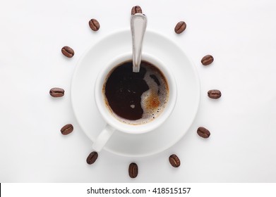 Coffee cup with spoon on saucer and coffee beans against white background forming clock dial. View from above. Coffee as symbol of morning energy and cheerfulness or evening refreshment.