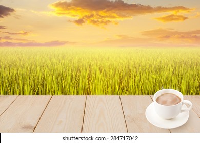 Coffee cup with wood texture on green rice field sunset.