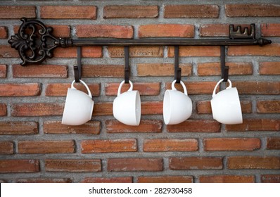 Coffee cups hanging on hooks in front of brick wall - Powered by Shutterstock