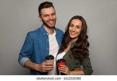 Coffee drinkers. Close-up photo of a wonderful woman in a khaki shirt and a handsome man in denim outfit, who are hugging, holding two coffee cups and smiling. - Powered by Shutterstock