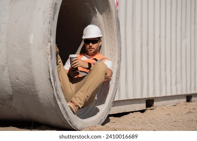 Coffee, engineer and construction worker relax on break at construction site. handsome male builder in hard hat smiling at camera. Construction Worker on Duty. Contractor and the Wooden House Frame - Powered by Shutterstock