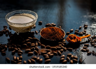 Coffee Face Mask For Treating Oily Skin And For Skin Whitening On A Black Colored Shiny Surface Consisting Of Some Coffee Beans Powder, Turmeric Powder, And Yogurt.