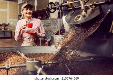 A Coffee Factory Worker Drinking Cup Of Coffee Next To A Roasting Machine In Facility.