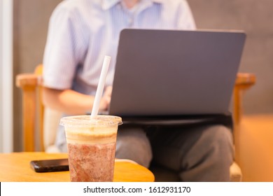 Coffee Frappuccino Blended With Paper Straw And Woman Using Laptop In Background.