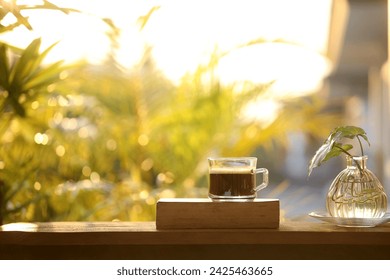 Coffee glass cup on thick old book on wooden table with plant glass vase under sunlight  - Powered by Shutterstock