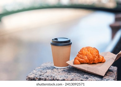 Coffee to go and fresh croissant on the promenadeon bavkground of Moika river