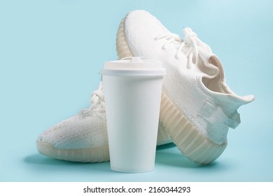 Coffee to go. White sneakers and a white paper cup with coffee on a blue background. Mockup - Shutterstock ID 2160344293