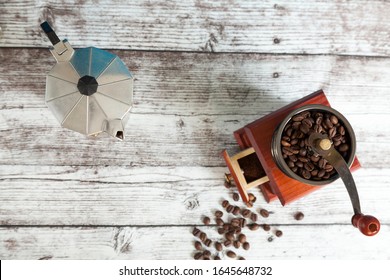 Coffee Grinder With Coffee Grains And Italian Coffee Maker On Wooden Table From Above. Top View