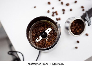Coffee grinder on white kitchen table. There are coffee beans on background.