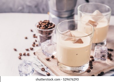 Coffee liqueur in glasses with ice and beans, wood background, copy space, toned