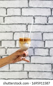 Coffee Macchiato And Milk Layer With Ice In Champagne Glass Was Held By Asian Grandmother Hand In Front Of White Brick Wall Wallpaper.