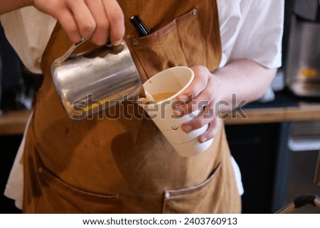  The coffee machine is frothing milk. Barista's hands hold a jug of milk.