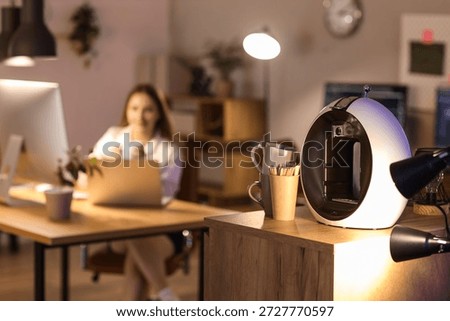 Coffee machine with stir sticks and cups on table in office at night, closeup