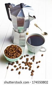 coffee maker with cup of coffee and coffee beans on wooden background