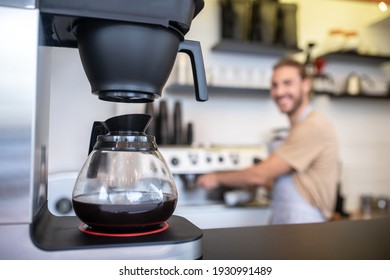 Coffee maker. Coffee maker with glass jug of coffee standing on counter and man at distance in coffee shop