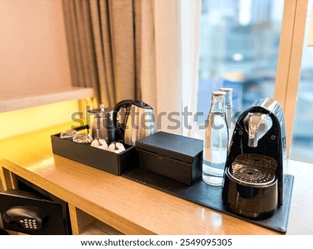 Coffee maker set equipment, with clean cup,spoon,drinking water and  electric kettle in a 5 star hotel room minibar or pantry overlooking a curtained window with city view.