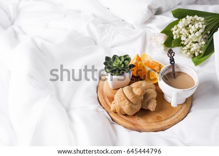 Coffee with milk and a bouquet of lilies of the valley in bed with a croissant and an orange. a place for the text