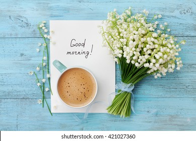 Кофейная кружка с букетом цветов ландыша и нотами доброго утра на бирюзовом деревенском столе сверху, красивый завтрак, винтажная открытка, вид сверху, плоская лежа