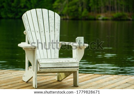 A coffee mug sitting on a white Adirondack chair on a wooden dock near the water.