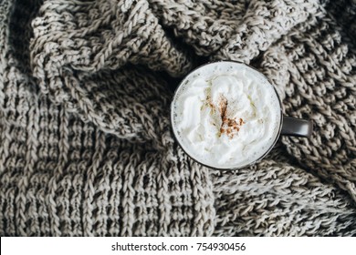Coffee mug with whipped cream and cinnamon powder on beige wool scarf. Flat lay, top view. Foto Stock