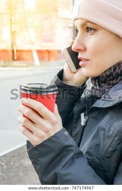 Coffee on the go. Autumn woman holding coffee\
while walking along the\
street