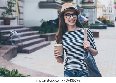 Coffee On The Go.  Beautiful Young Woman Holding Coffee Cup And Smiling While Walking Along The Street