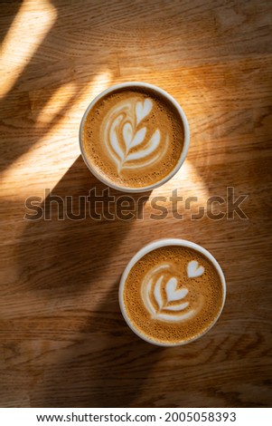 Coffee on wooden background. Two cups of cappuccino with latte art on brown table with sunbeam. Fresh morning coffee with delicious milk foam. Top view, flat lay.