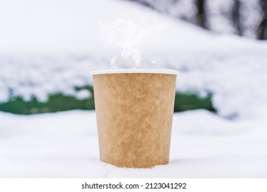 Coffee in a paper cup on a snowy winter background. Hot drink in cold weather.